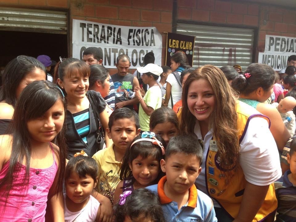 Lion Alexandra smiles with a big group of children during a community service project.